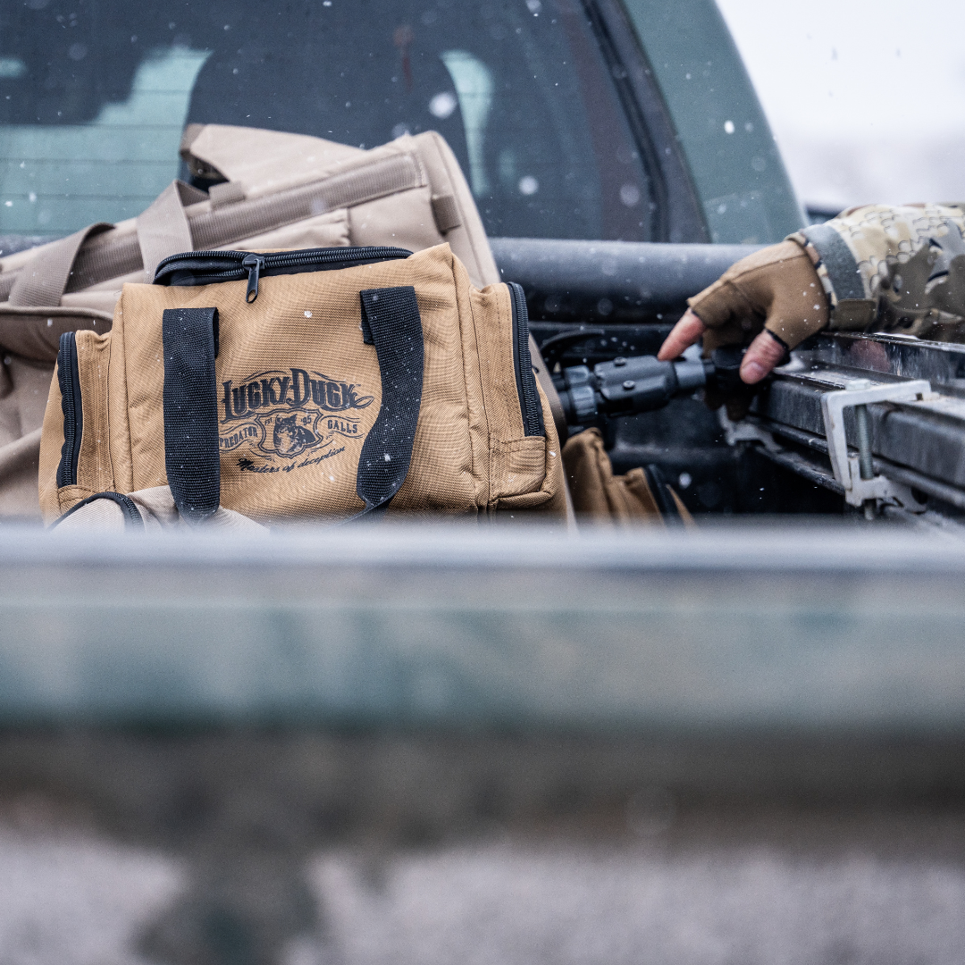 Tan E-Caller Bag with black logo and text on a vehicle's open door, with a person in camouflage gloves interacting with equipment.