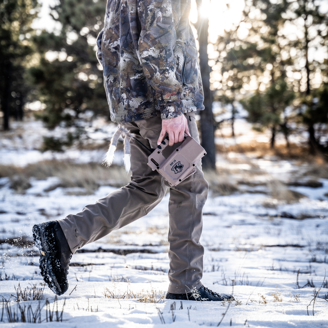 Person in camouflage jacket and pants walking in a snowy forest holding a Lucky Duck Riot 2.0 E-Caller