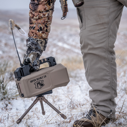 Hunting scene with a person in camouflage gear and a device labeled Lucky Duck Super Revolt 2.0 in a snowy landscape.