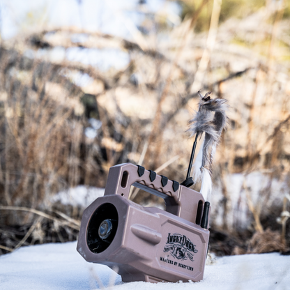 Hunting call device with feathers on a snowy ground and blurred natural background